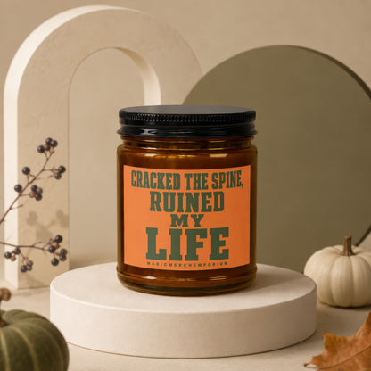 Candle with "CRACKED THE SPINE, RUINED MY LIFE" text on orange label.