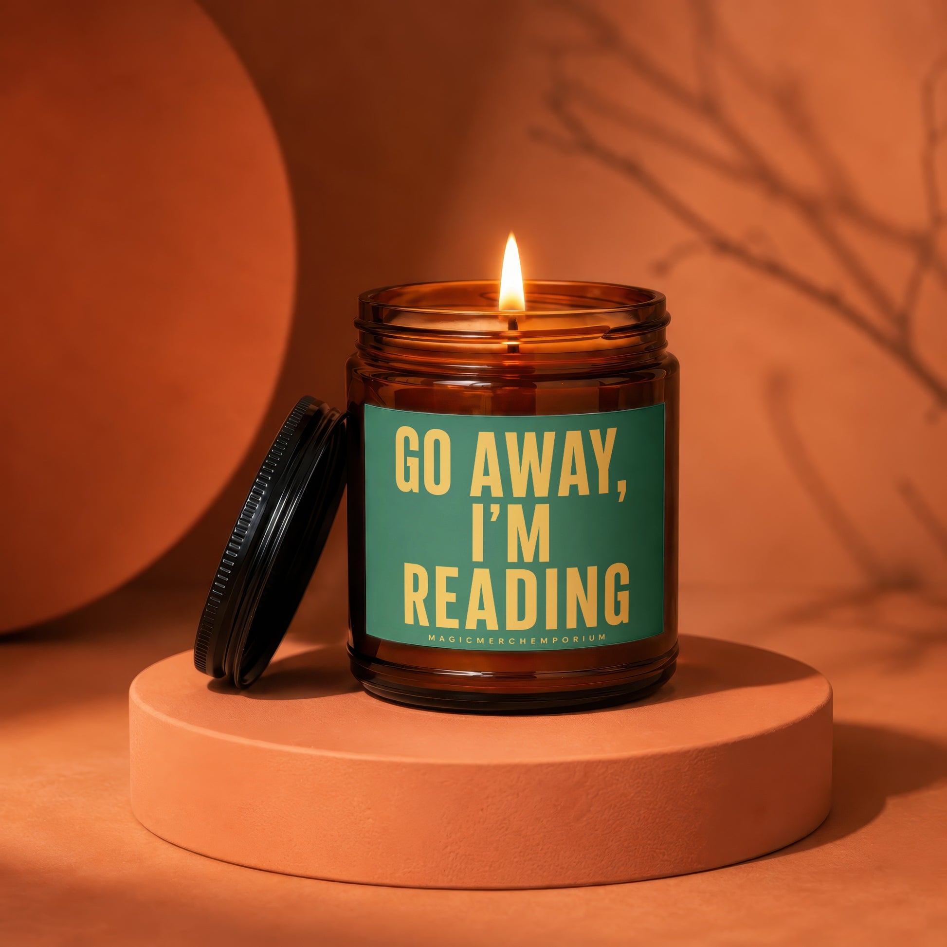 Burning amber glass candle with green label reading "GO AWAY, I'M READING".