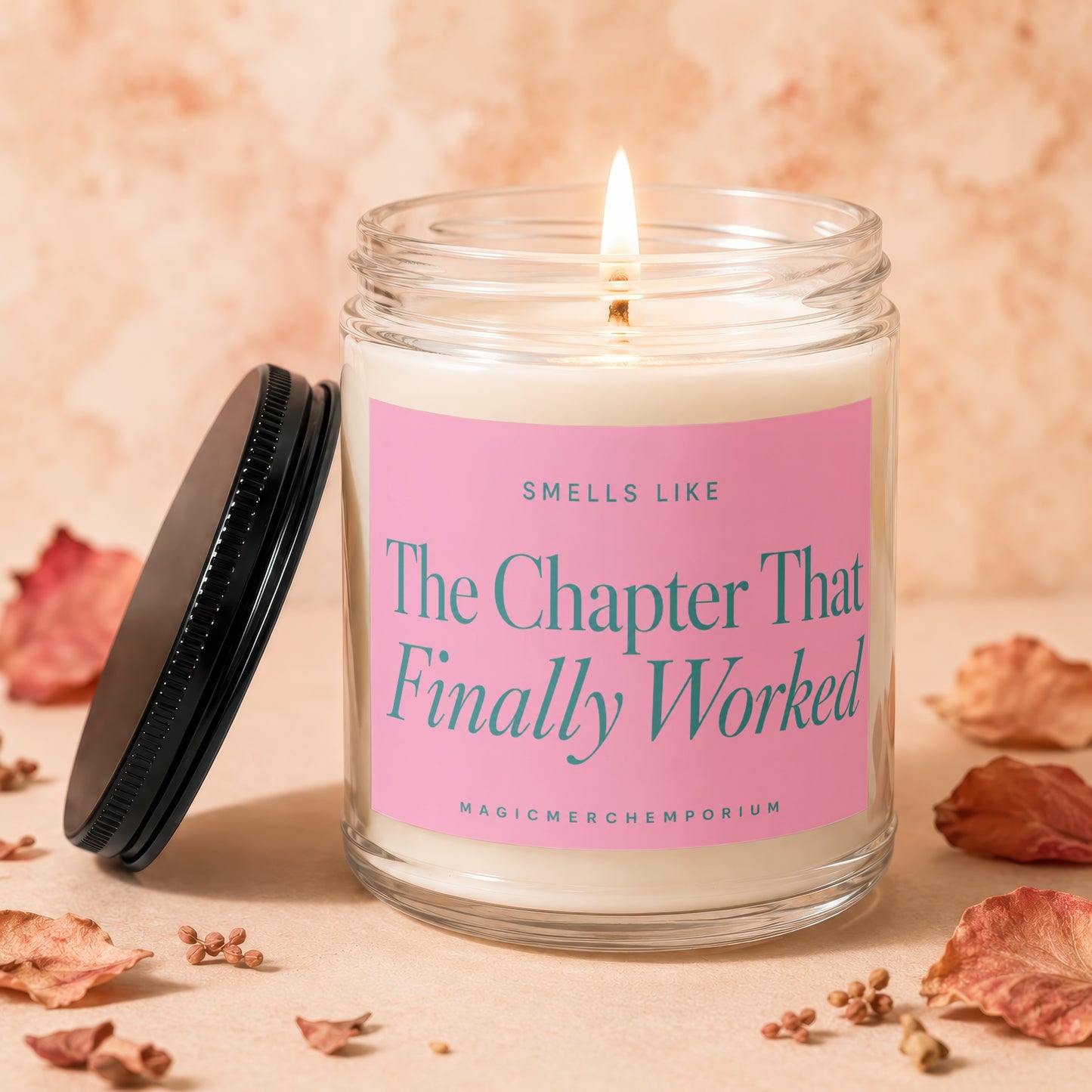 Lit candle in glass jar with pink label reading "The Chapter That Finally Worked".