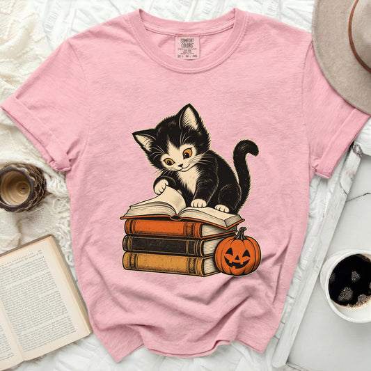 Pink t-shirt with a black and white kitten sitting on books and a pumpkin.