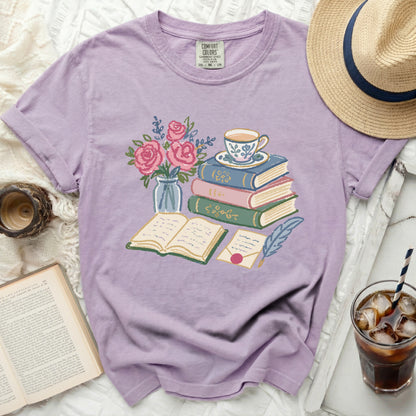 Purple t-shirt with graphic of stacked books, teacup, flowers, and letter.