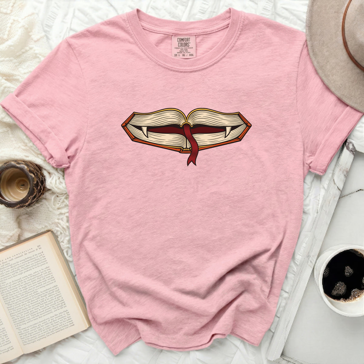 Pink t-shirt with an open book graphic featuring fangs and a red ribbon.