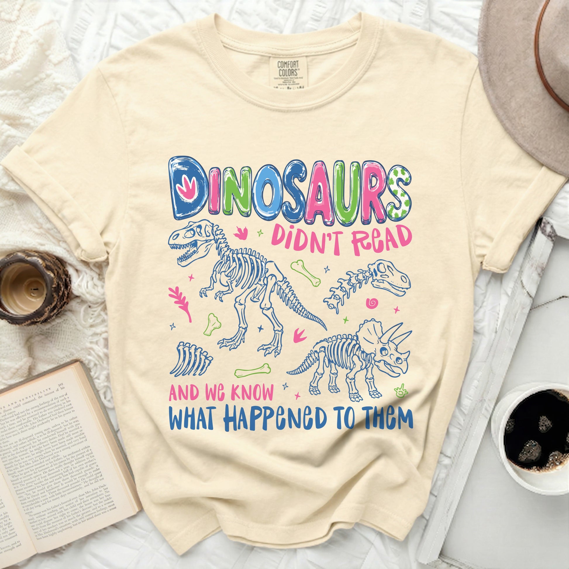 Cream t-shirt with "DINOSAURS DIDN'T READ AND WE KNOW WHAT HAPPENED TO THEM" graphic.