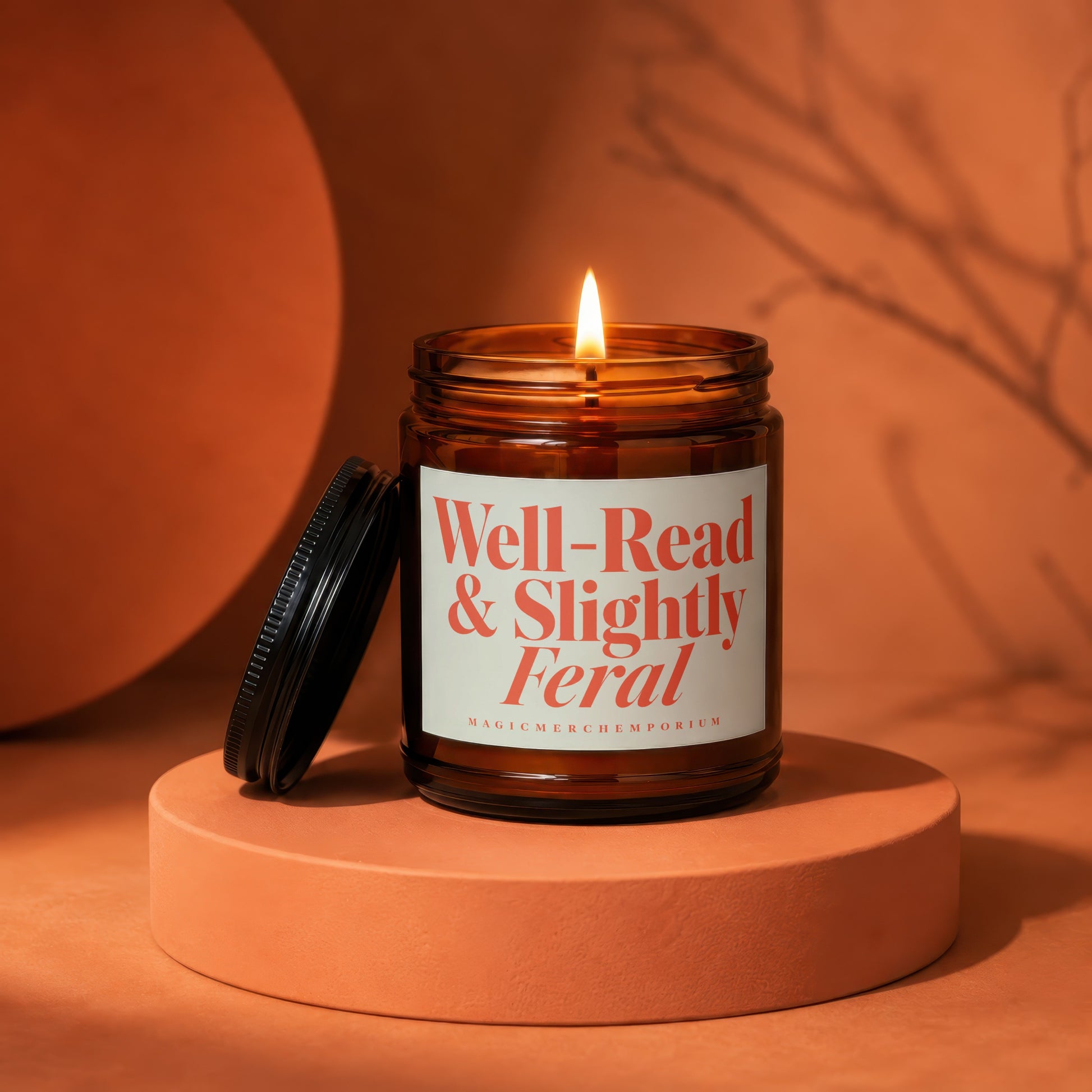 Lit amber glass candle with "Well-Read & Slightly Feral" label on orange pedestal.