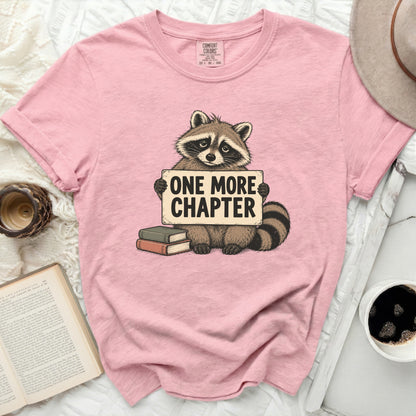 Pink t-shirt with a raccoon holding a sign that says "ONE MORE CHAPTER".