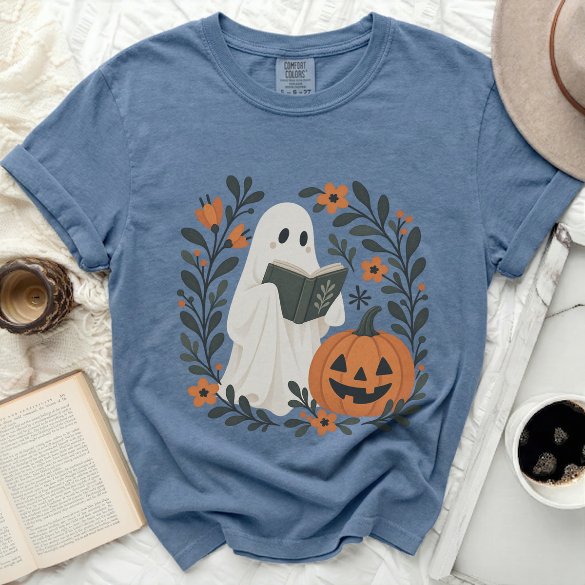Ghost reading a book surrounded by fall flowers and a pumpkin.