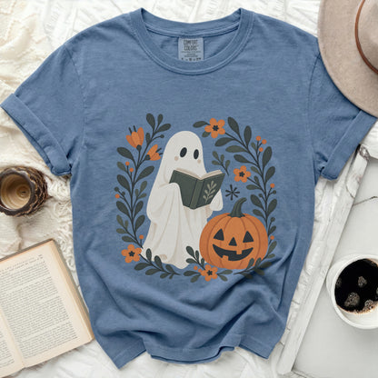 Ghost reading a book surrounded by fall flowers and a pumpkin.