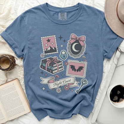 Blue t-shirt with pastel graphic of moon, books, bats, key, and "Night Court" text.
