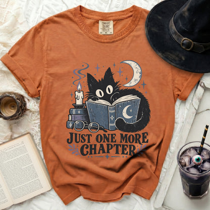 Orange t-shirt with black cat reading books, crescent moon, stars, candle, and text "JUST ONE MORE CHAPTER".