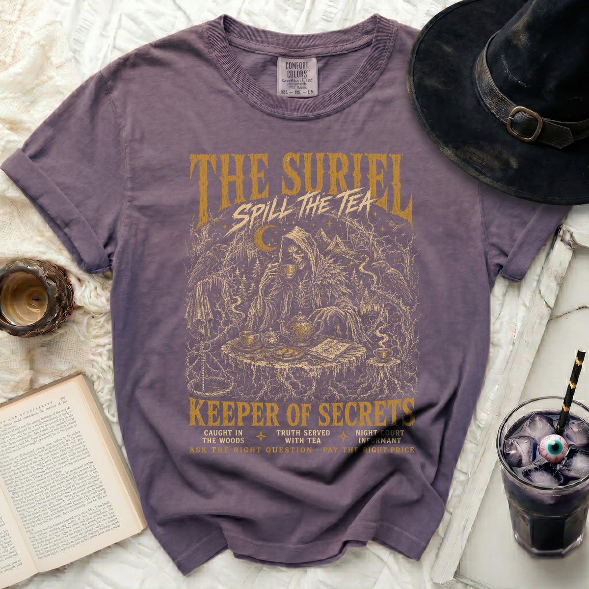 Purple t-shirt with "The Suriel Spill The Tea Keeper of Secrets" gold graphic.