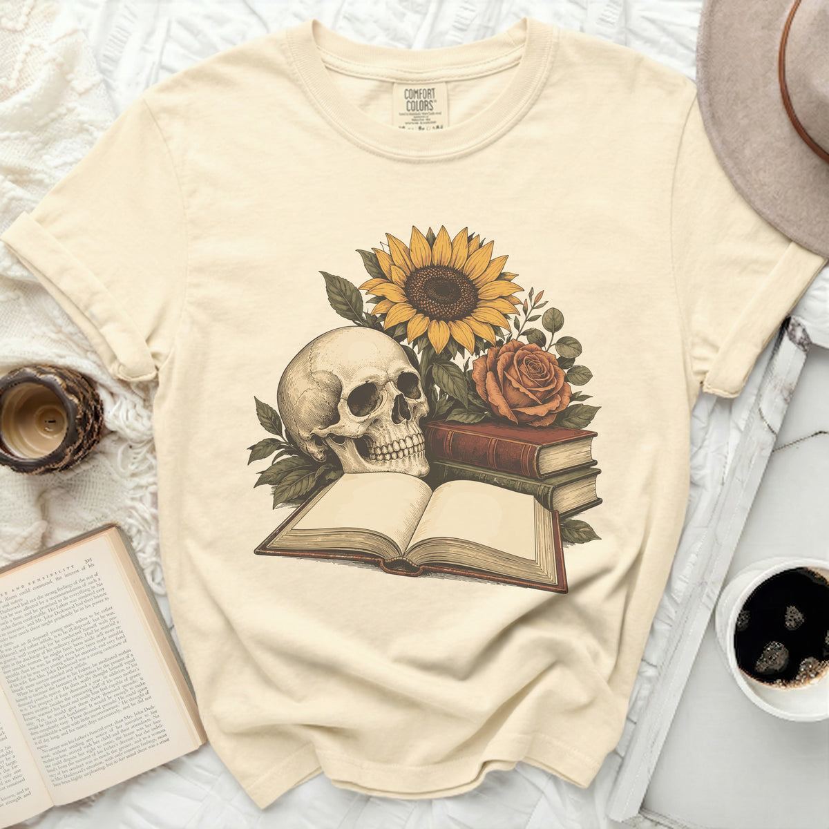 Skull, sunflower, rose, and books graphic on a cream t-shirt.