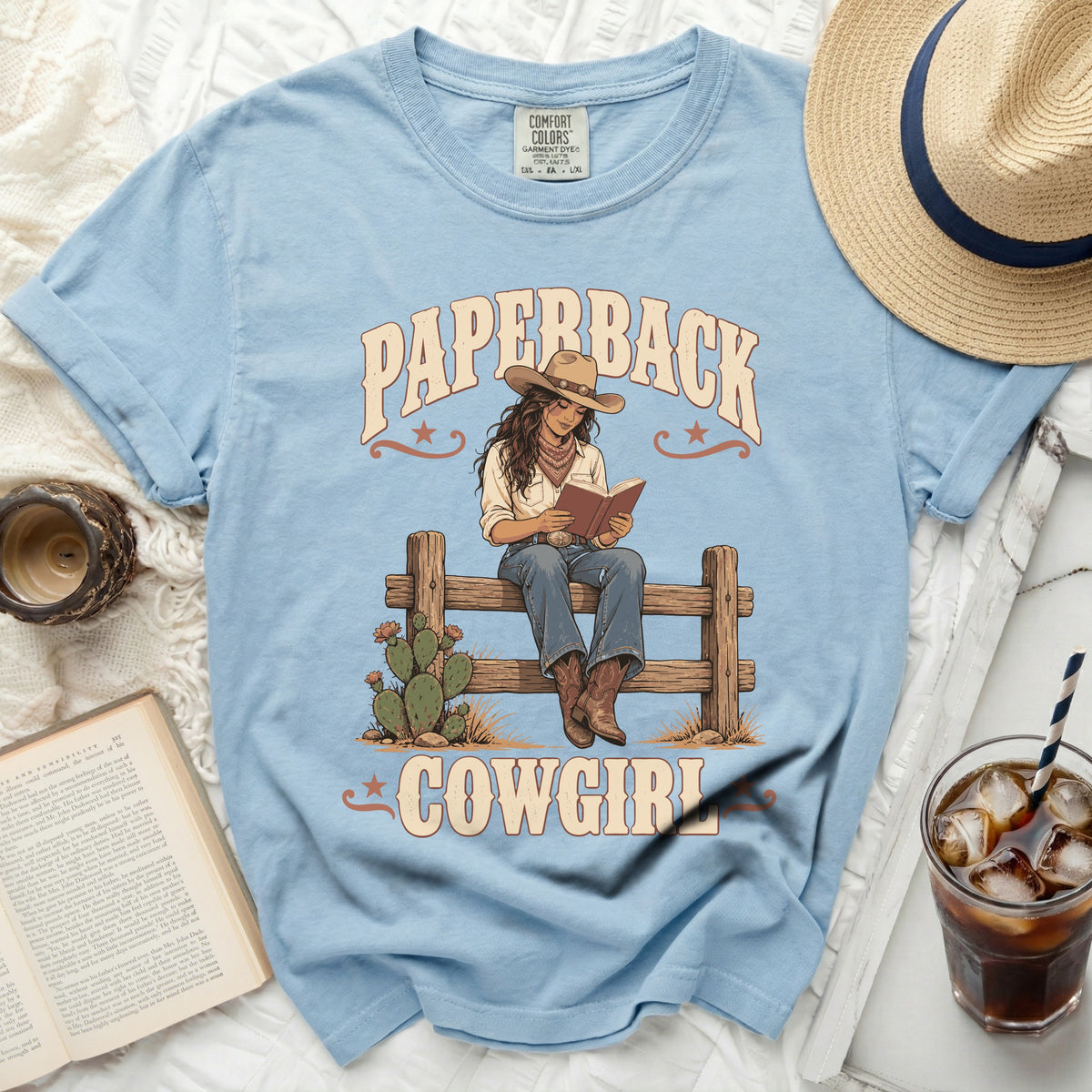 Light blue t-shirt with "Paperback Cowgirl" graphic of woman reading on fence.