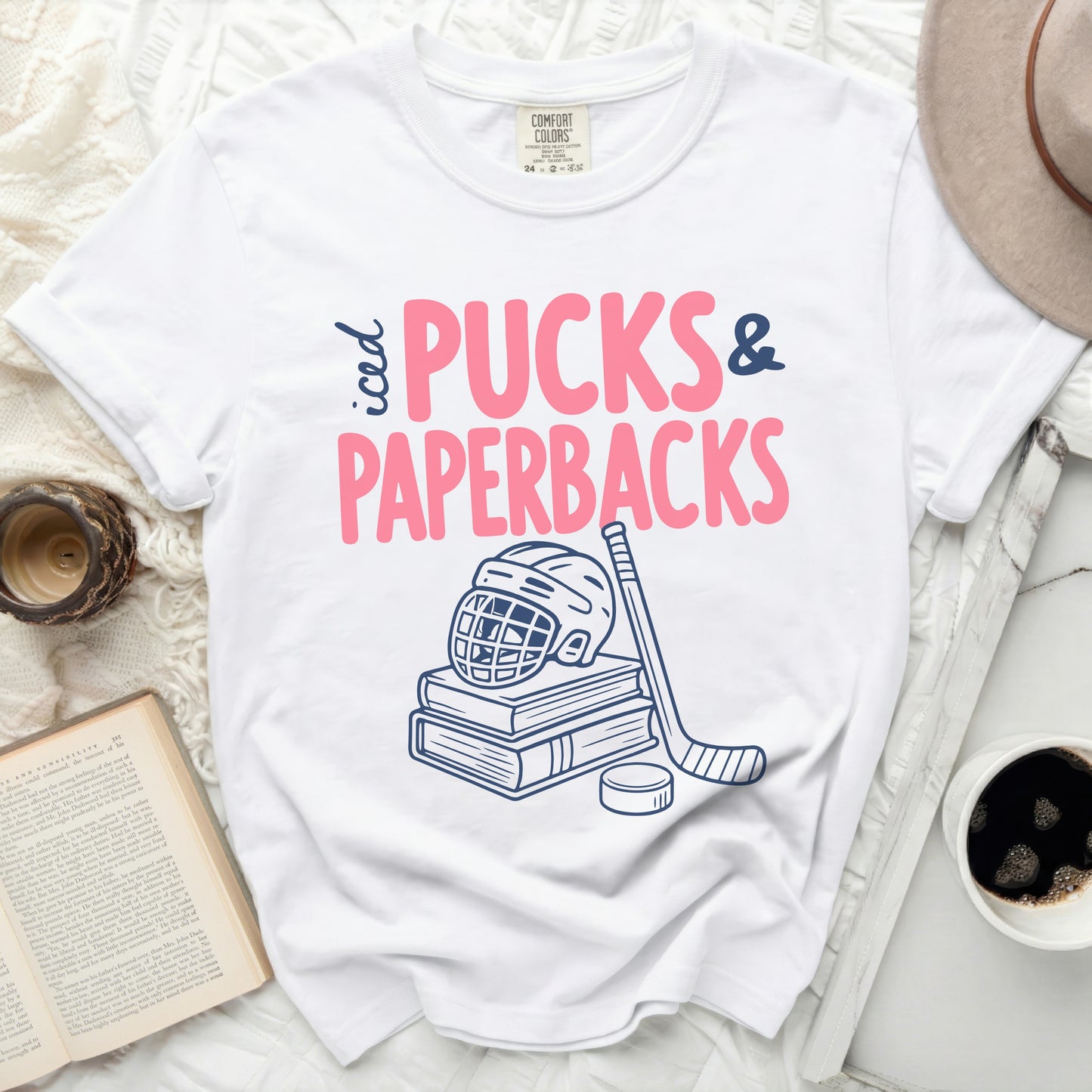 White t-shirt with "iced PUCKS & PAPERBACKS" text, hockey stick, and puck.