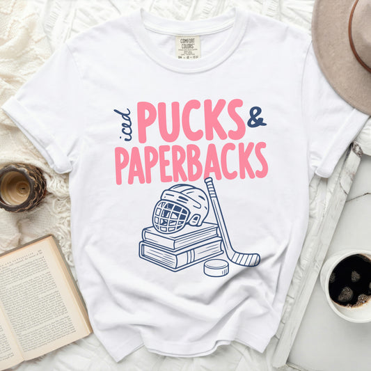 White t-shirt with "iced PUCKS & PAPERBACKS" text, hockey stick, and puck.