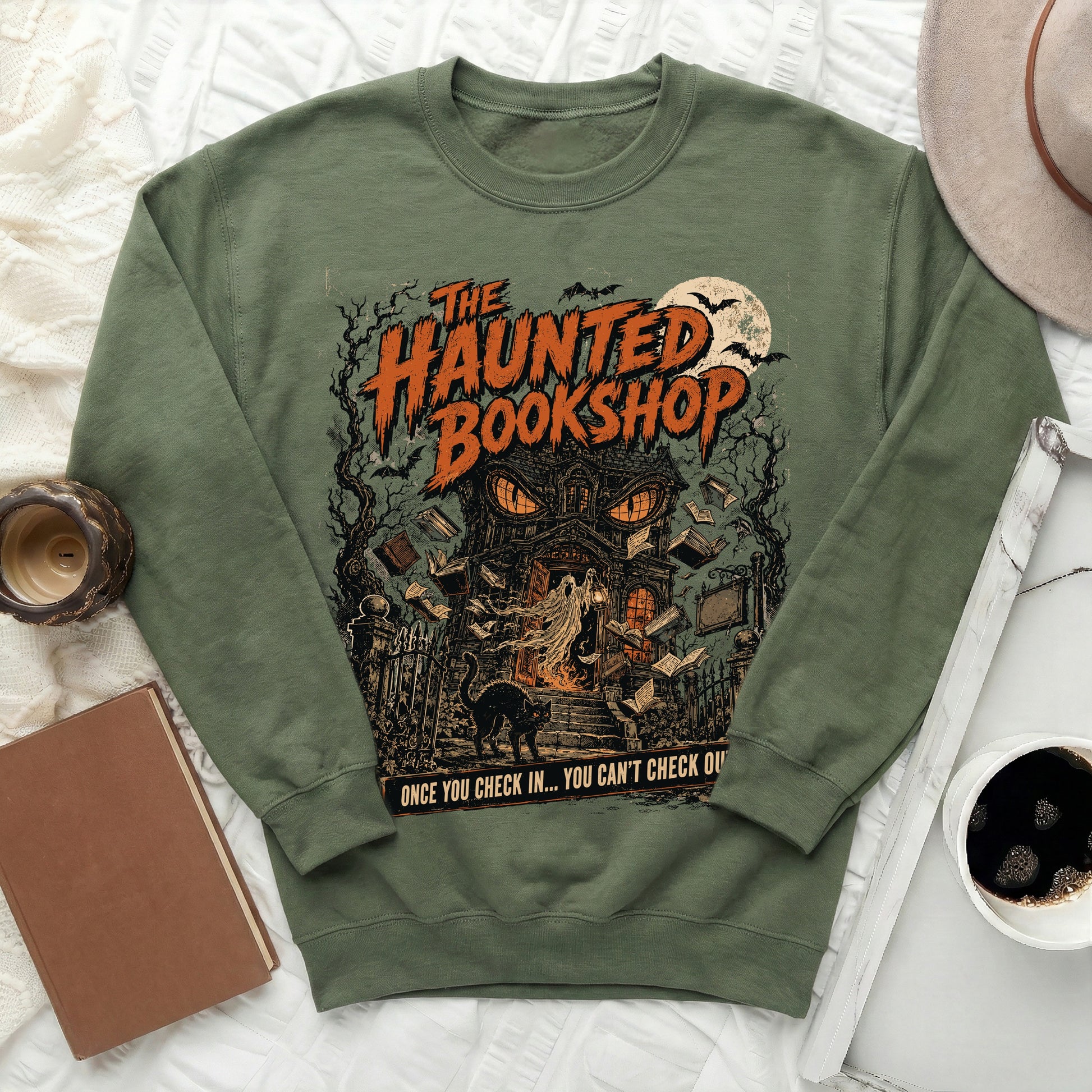 Olive green sweatshirt with "The Haunted Bookshop" graphic, ghost, black cat, and quote.