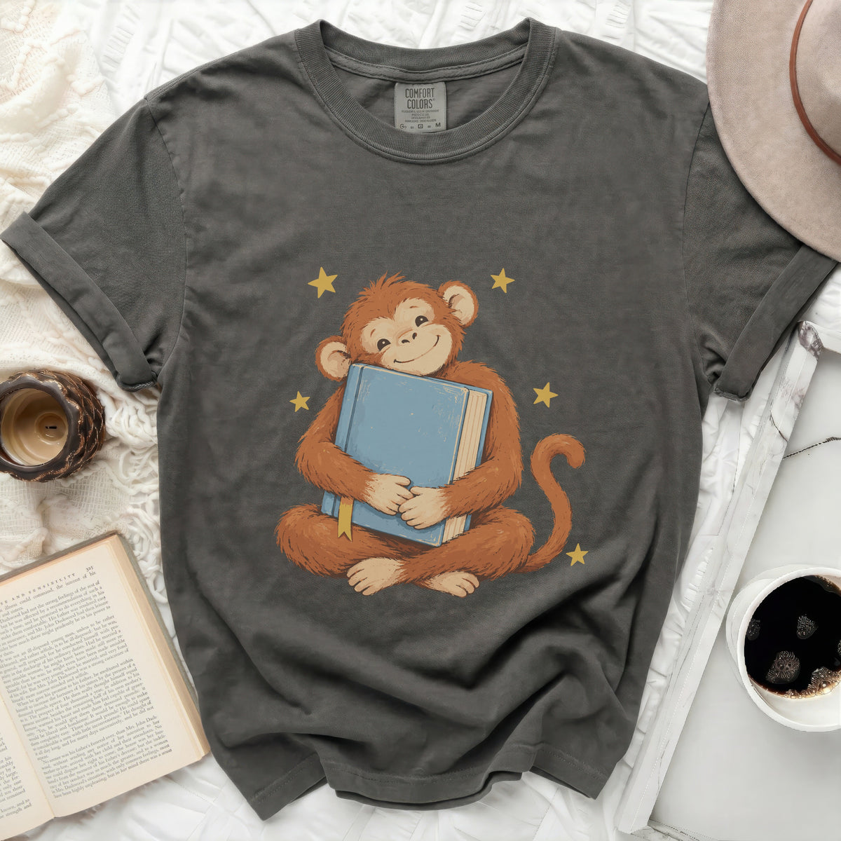 Grey t-shirt with a graphic of a smiling monkey hugging a blue book and yellow stars.