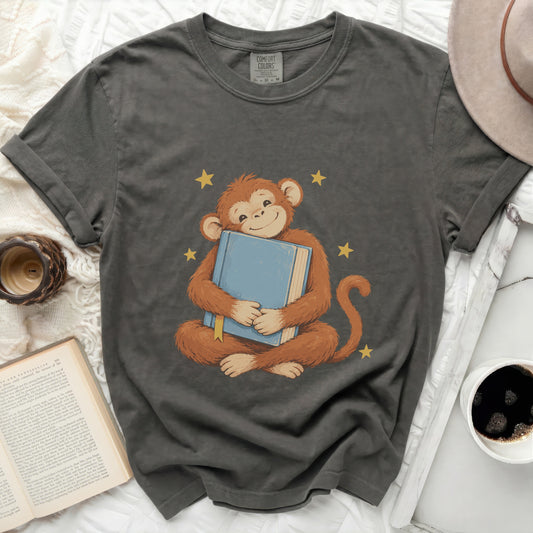 Grey t-shirt with a graphic of a smiling monkey hugging a blue book and yellow stars.