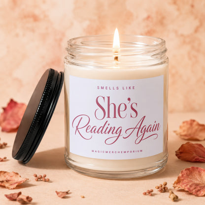 Scented candle with lit wick and label reading "Smells Like She's Reading Again".