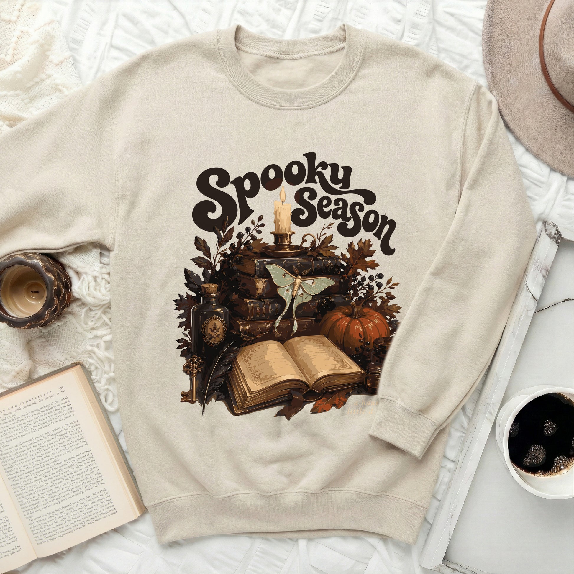 Cream sweatshirt with "Spooky Season" graphic featuring books, candle, and moth.