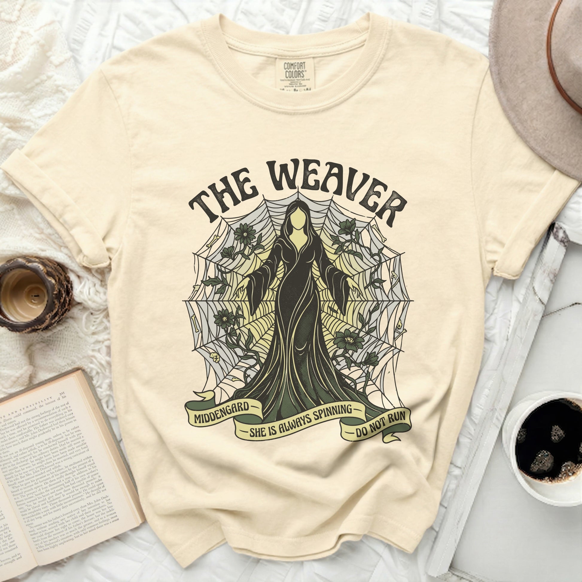 Cream t-shirt with "The Weaver" and spiderweb design, featuring a cloaked figure.