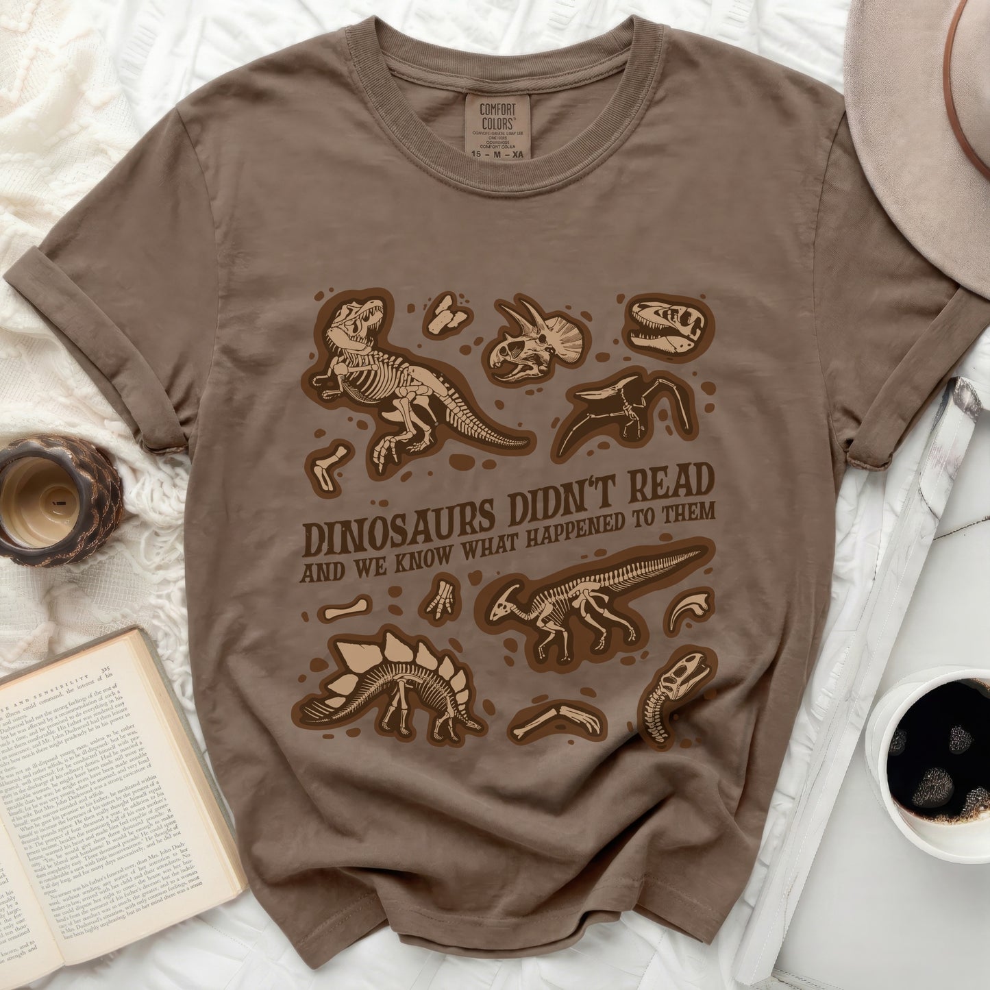 Brown t-shirt with brown dinosaur skeletons and text "DINOSAURS DIDN'T READ AND WE KNOW WHAT HAPPENED TO THEM".
