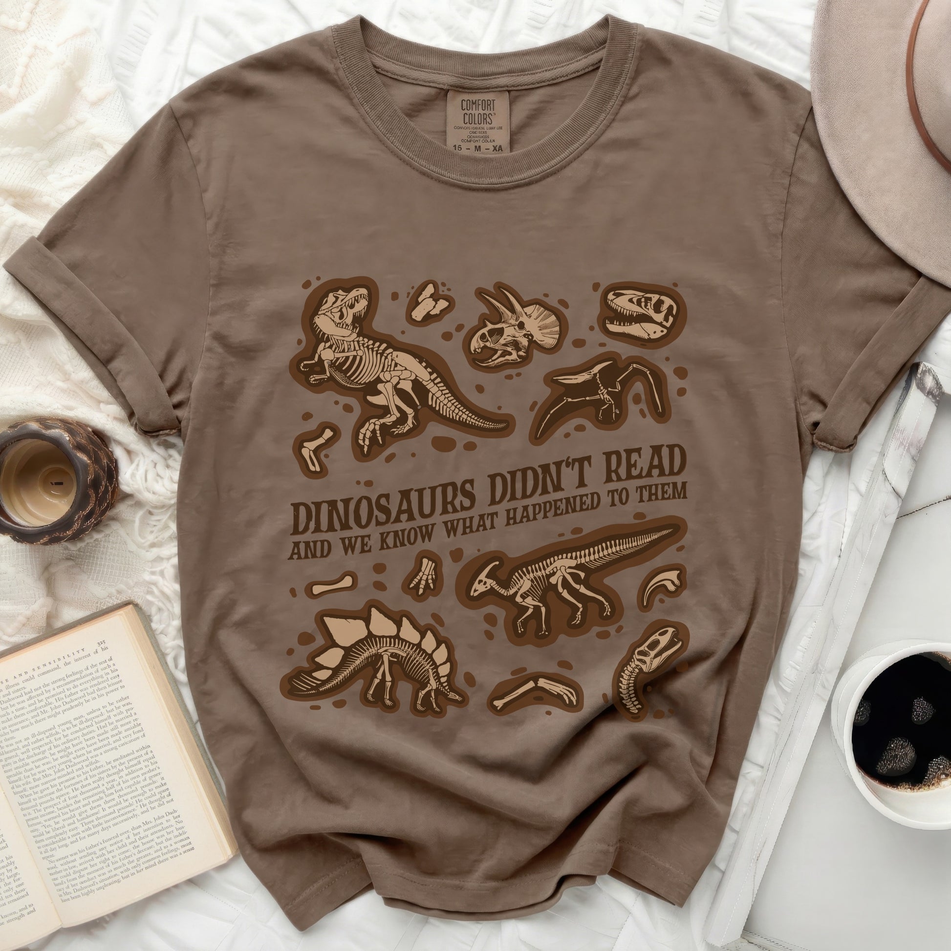 Brown t-shirt with brown dinosaur skeletons and text "DINOSAURS DIDN'T READ AND WE KNOW WHAT HAPPENED TO THEM".