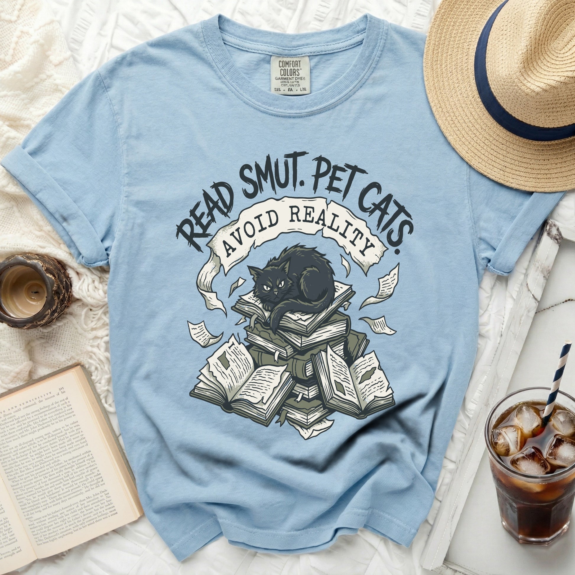 Light blue t-shirt with black cat on books and text "Read Smut. Pet Cats. Avoid Reality."