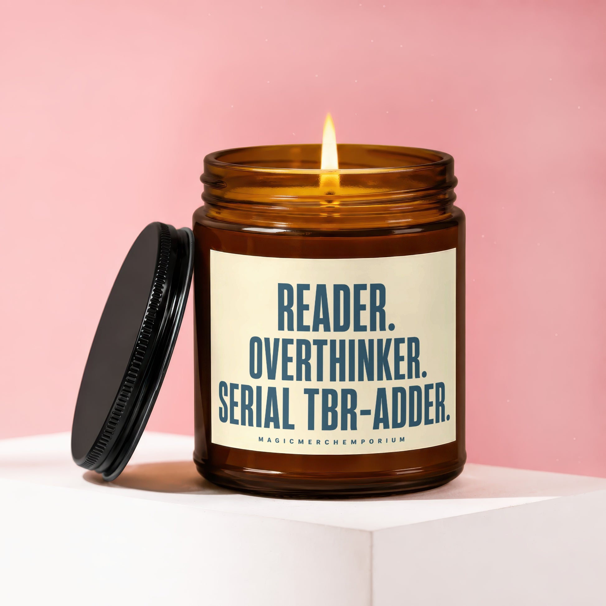 Amber jar candle with lit wick, lid off, reading "Reader. Overthinker. Serial TBR-Adder."