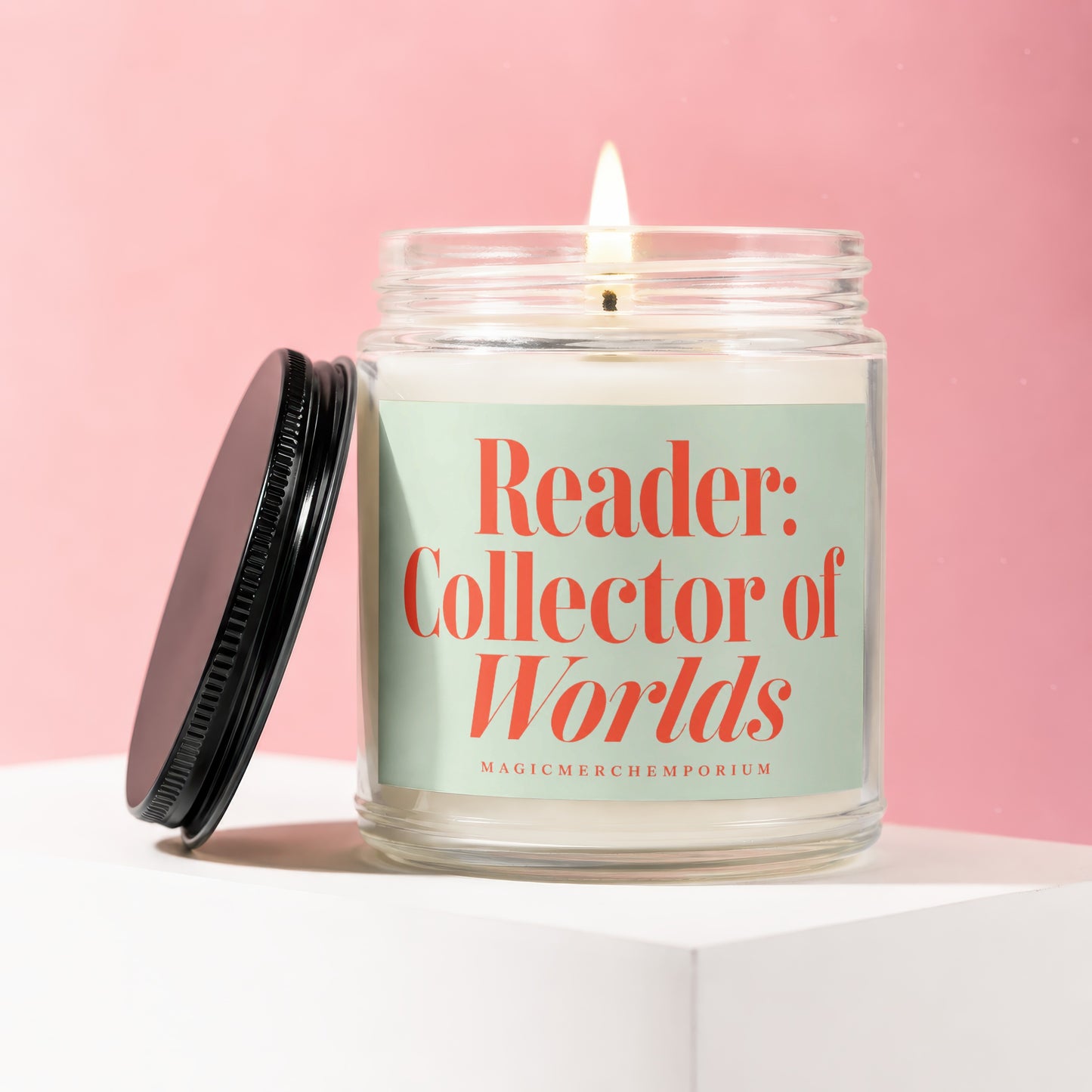 Lit candle in glass jar with black lid, reading "Reader: Collector of Worlds"