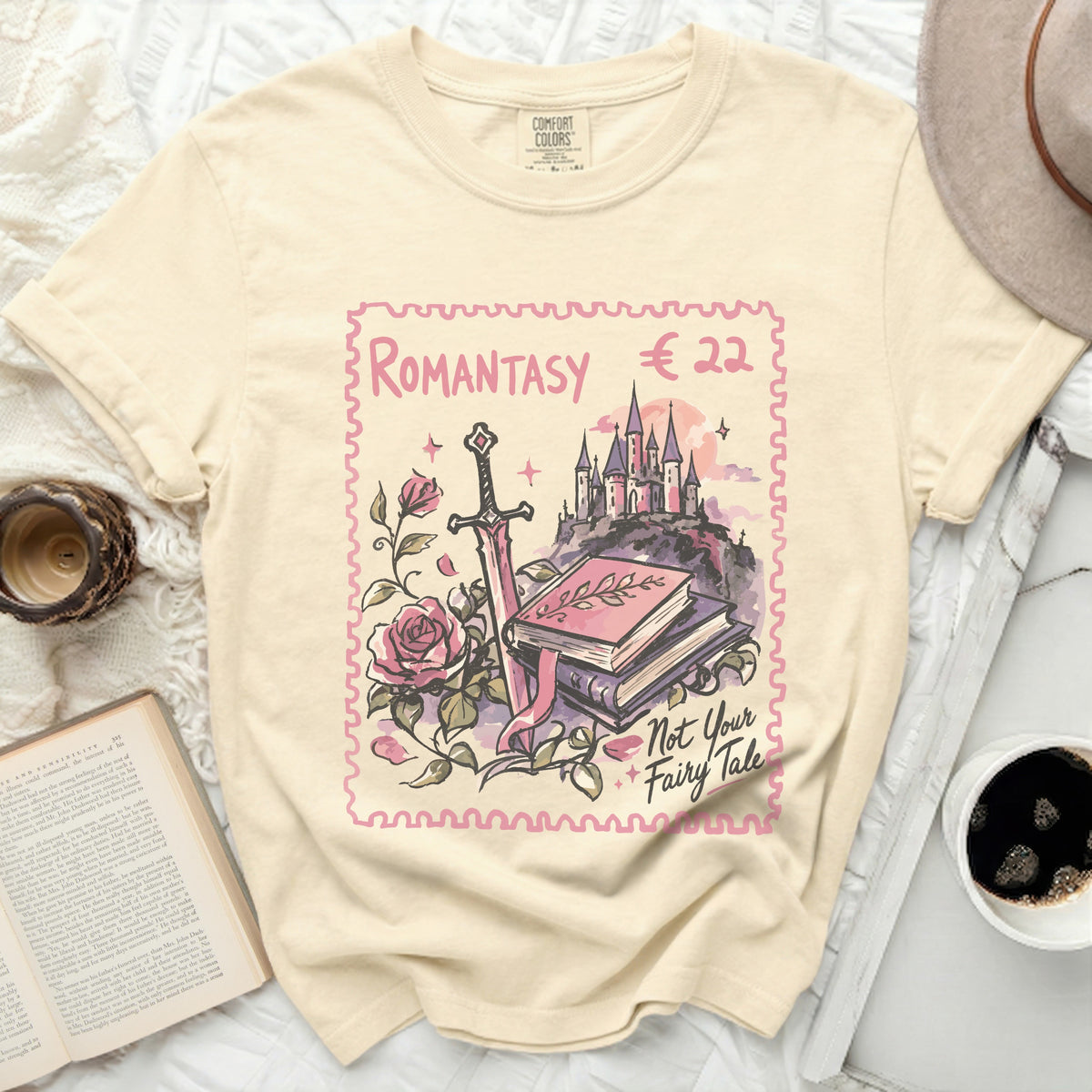 Cream t-shirt with a stamp design of a castle, sword, roses, and books.