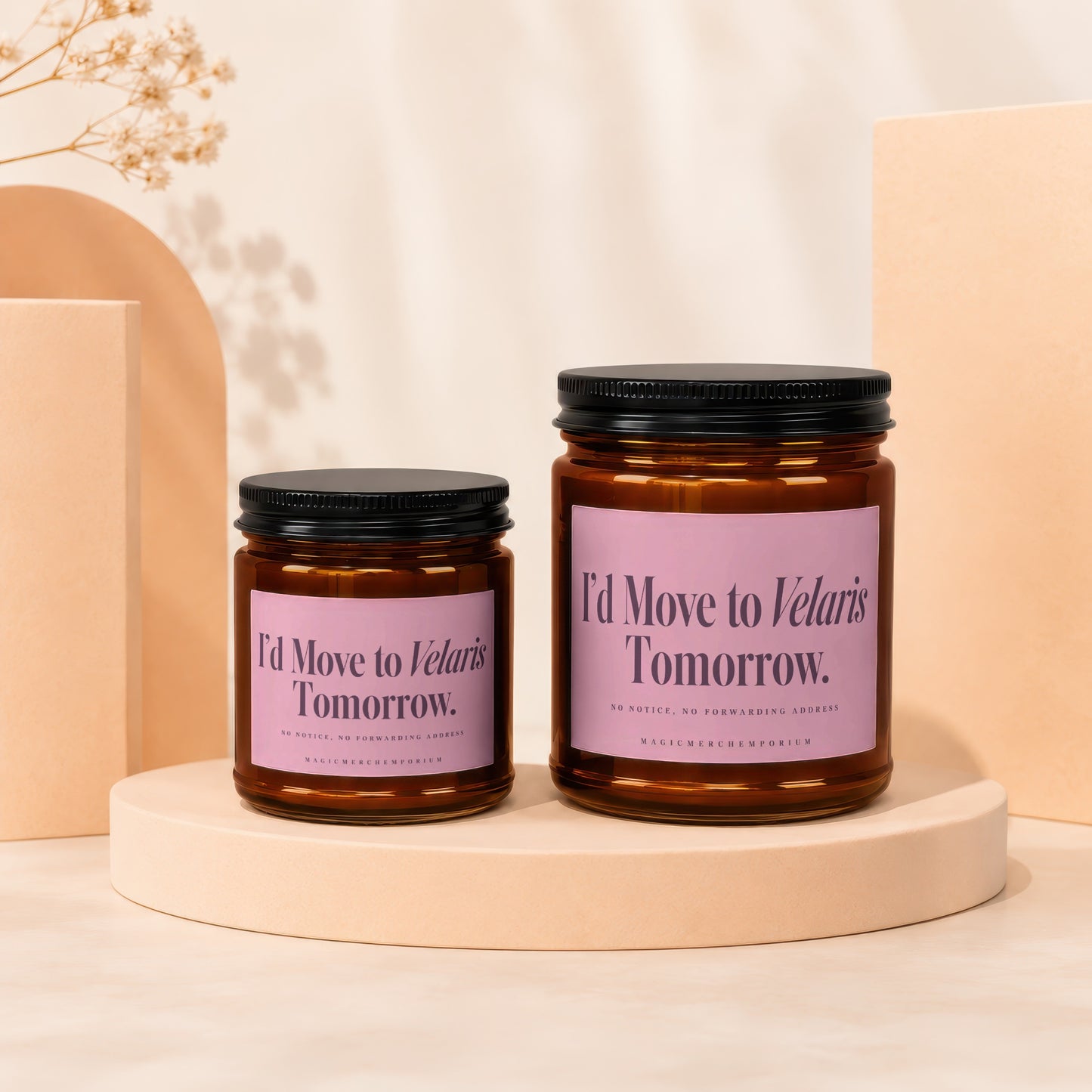 Two amber glass candles with pink labels reading I'd Move to Velaris Tomorrow stand on a beige pedestal.