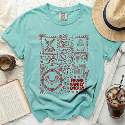 Teal t-shirt with red graphic design of swords, books, cauldron, hearts, and text.