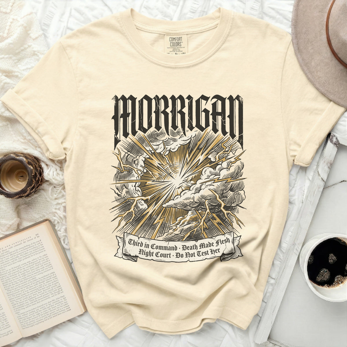 Cream t-shirt with black and gold "Morrigan" graphic and text.