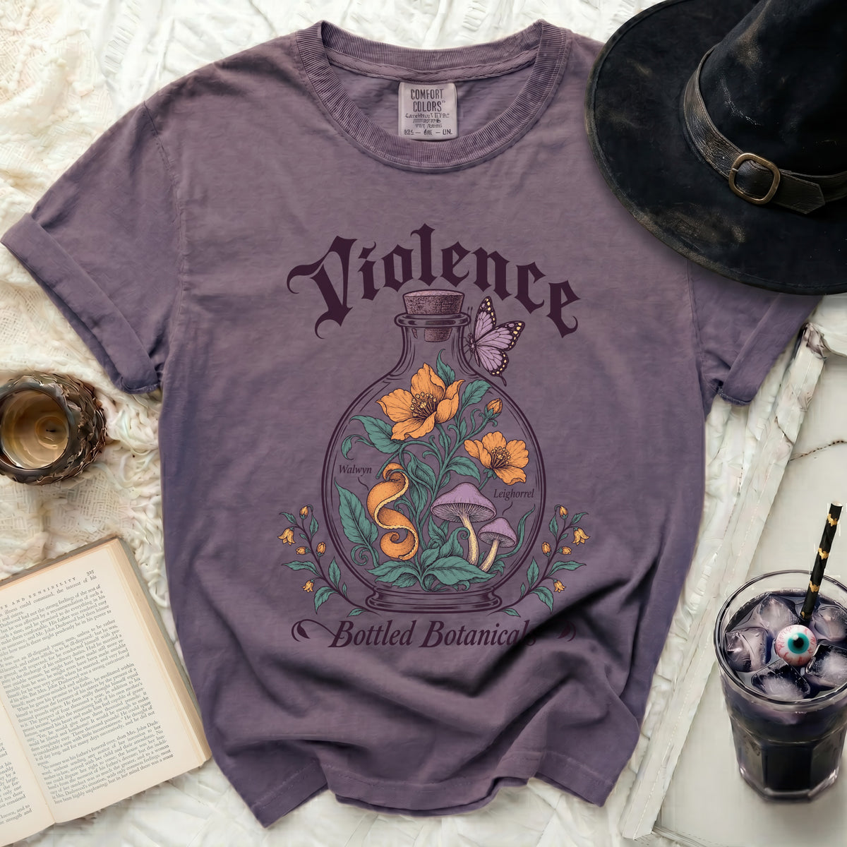 Purple t-shirt featuring a vintage botanical graphic with flowers, mushrooms, a snake, and the text Violence Bottled Botanicals.