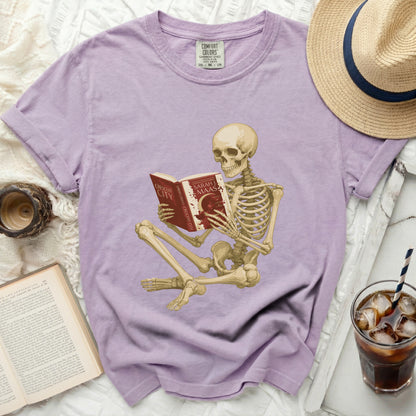 Skeleton reading a book titled "House of Earth and Blood" on a purple tee.