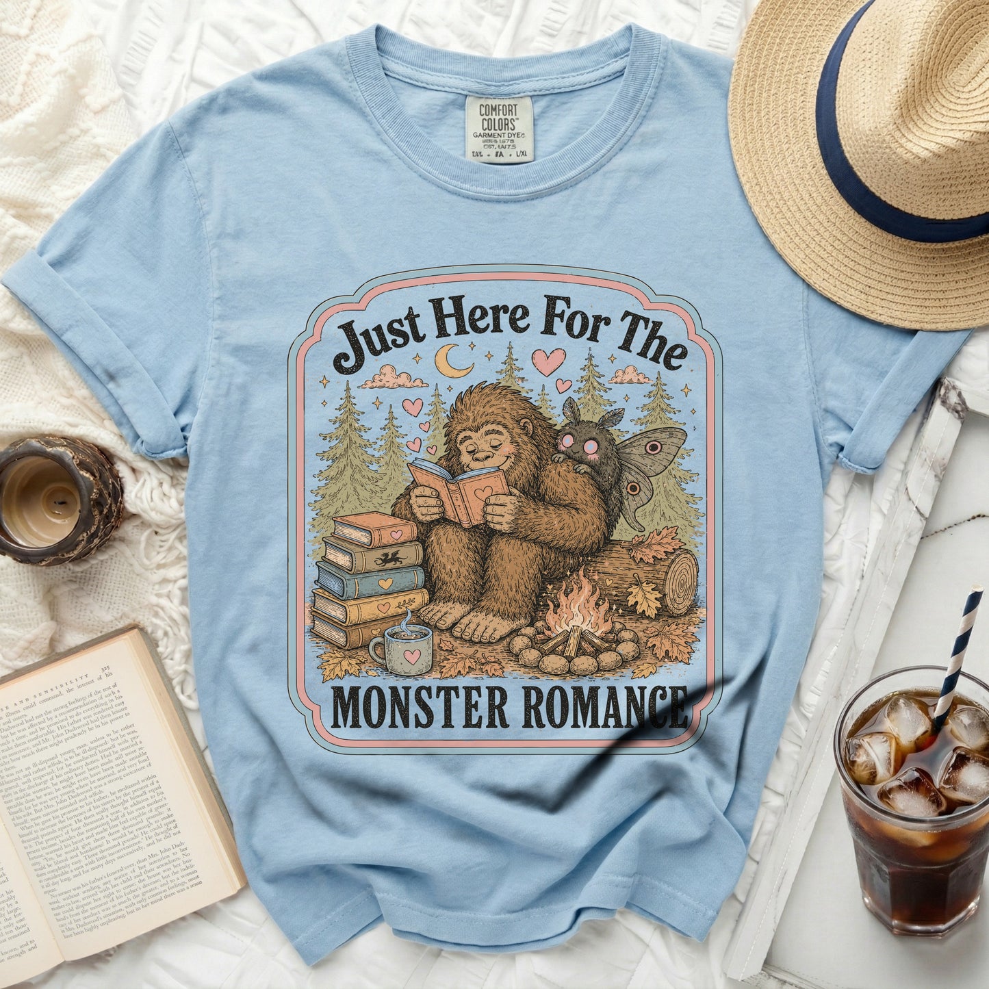 Bigfoot and moth reading by campfire with "Monster Romance" text.