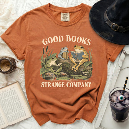Orange t-shirt with frogs reading books and text "GOOD BOOKS STRANGE COMPANY."