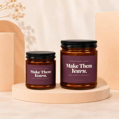 Two amber glass candles with dark lids and purple labels reading "Make Them Yearn."