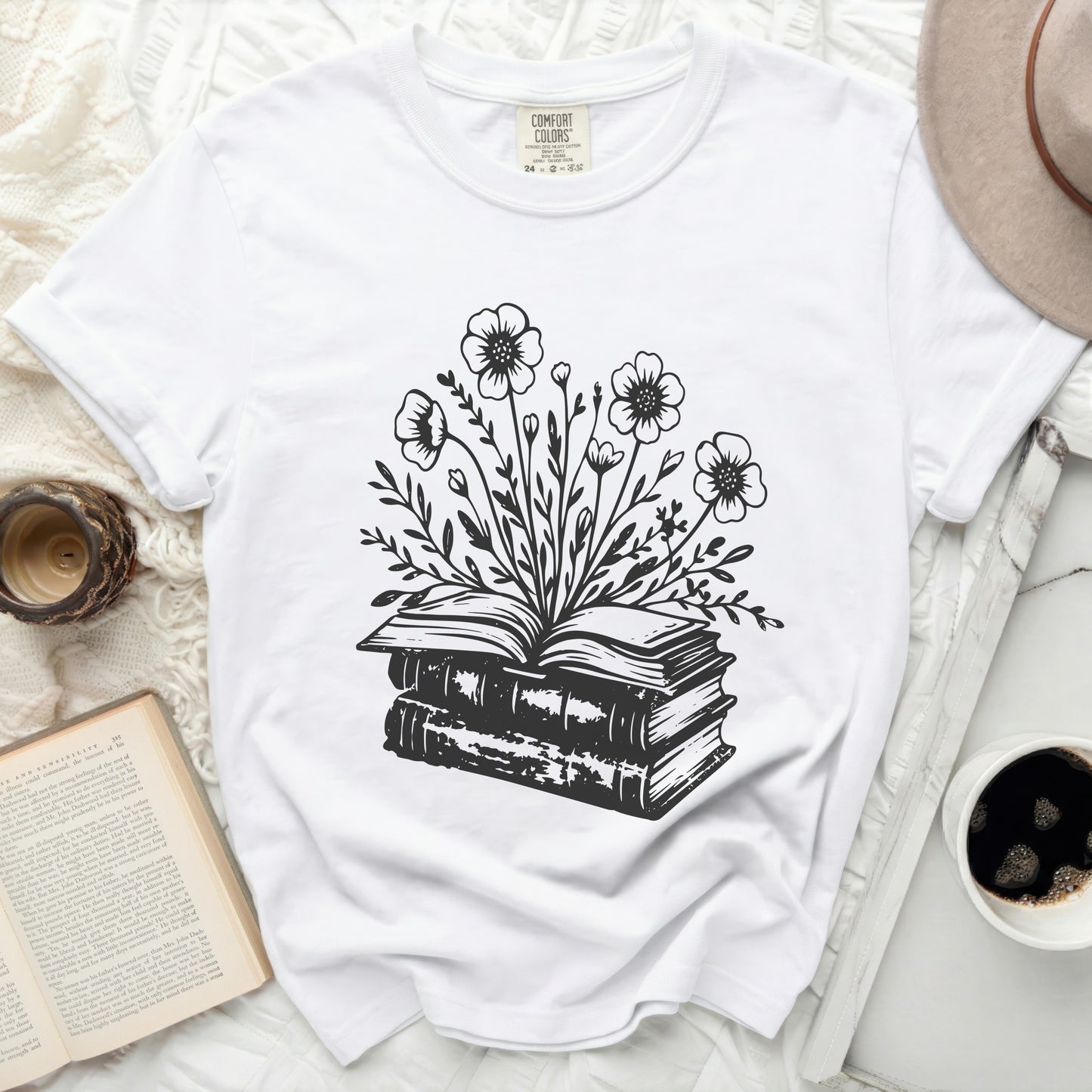 White t-shirt with black ink drawing of an open book crowned with flowers.