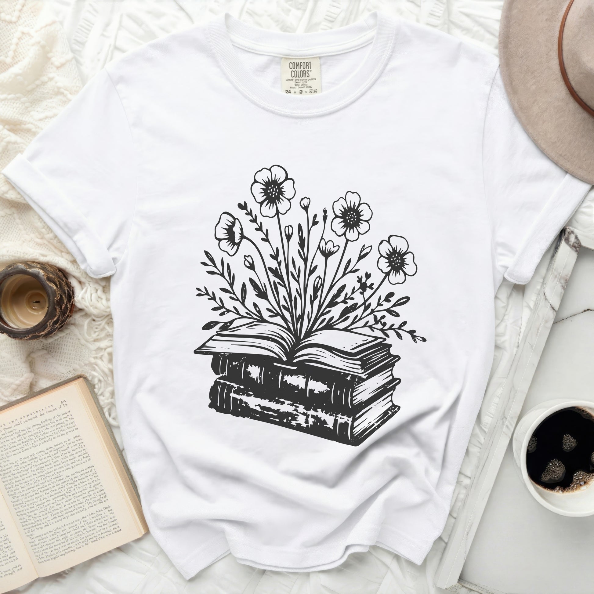White t-shirt with black ink drawing of an open book crowned with flowers.