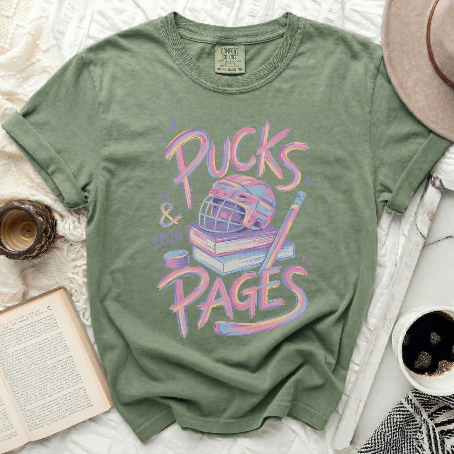 Green t-shirt with "Pucks & Pages 2026" text and hockey gear on books.
