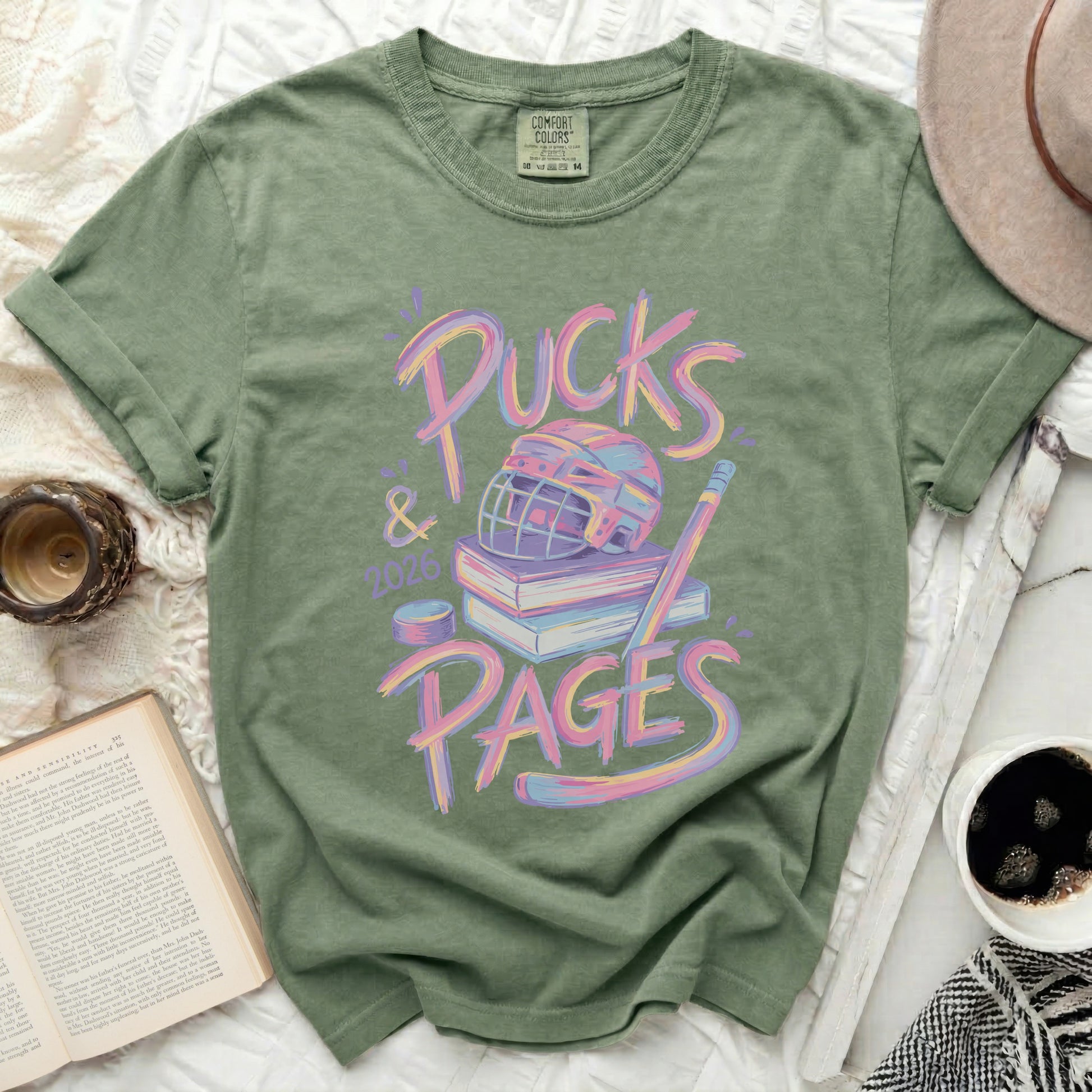 Green t-shirt with "Pucks & Pages 2026" text and hockey gear on books.