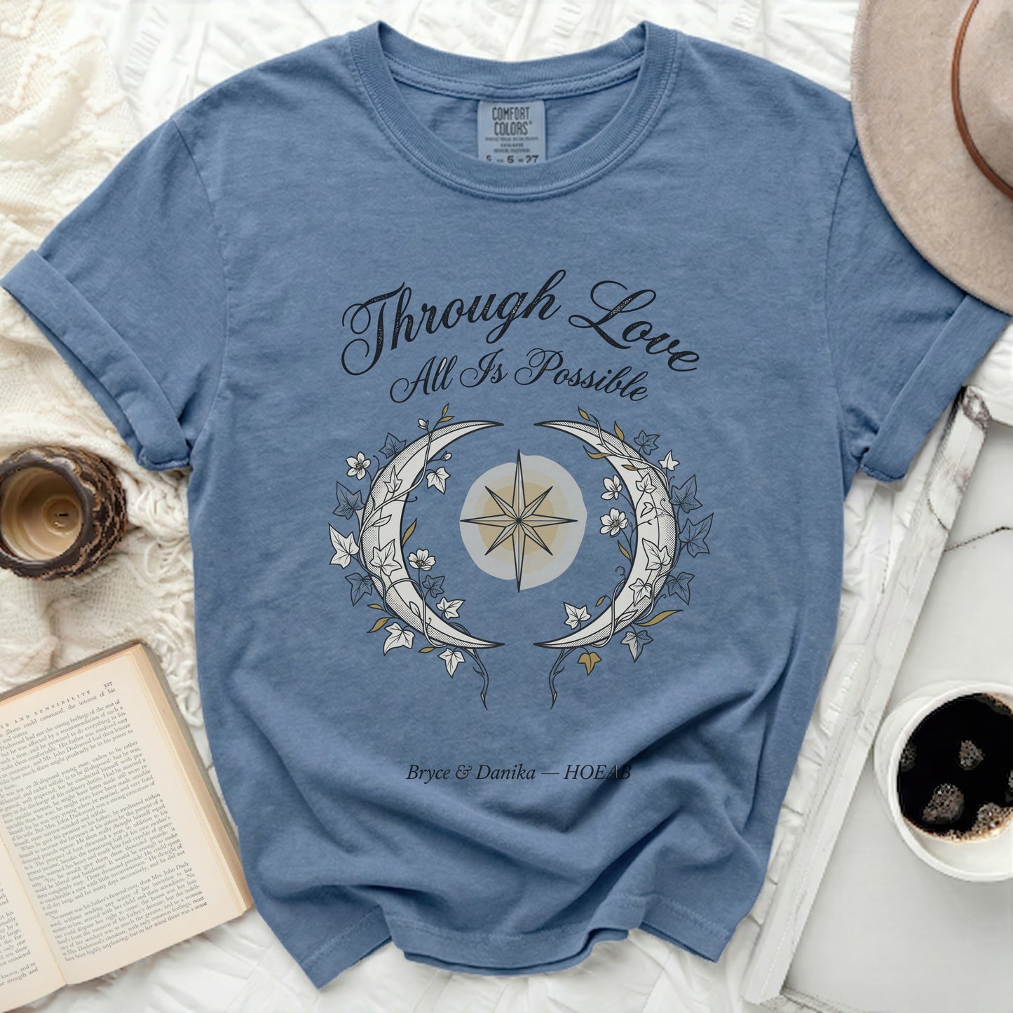 Blue t-shirt with "Through Love All Is Possible" and crescent moon design.
