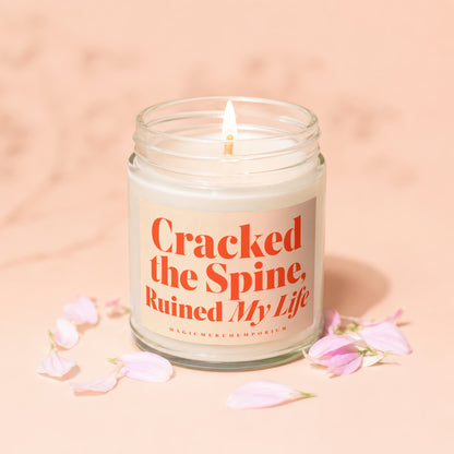 Candle with "Cracked the Spine, Ruined My Life" text on label and pink petals.
