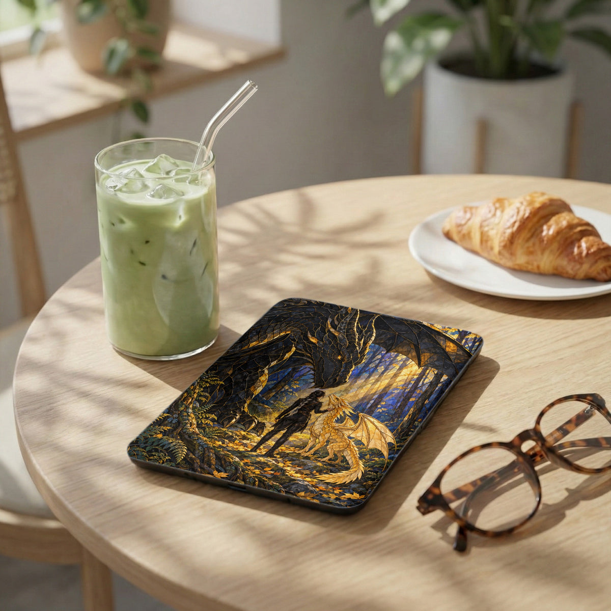 Case with woman and dragon art, next to matcha, croissant, and glasses.
