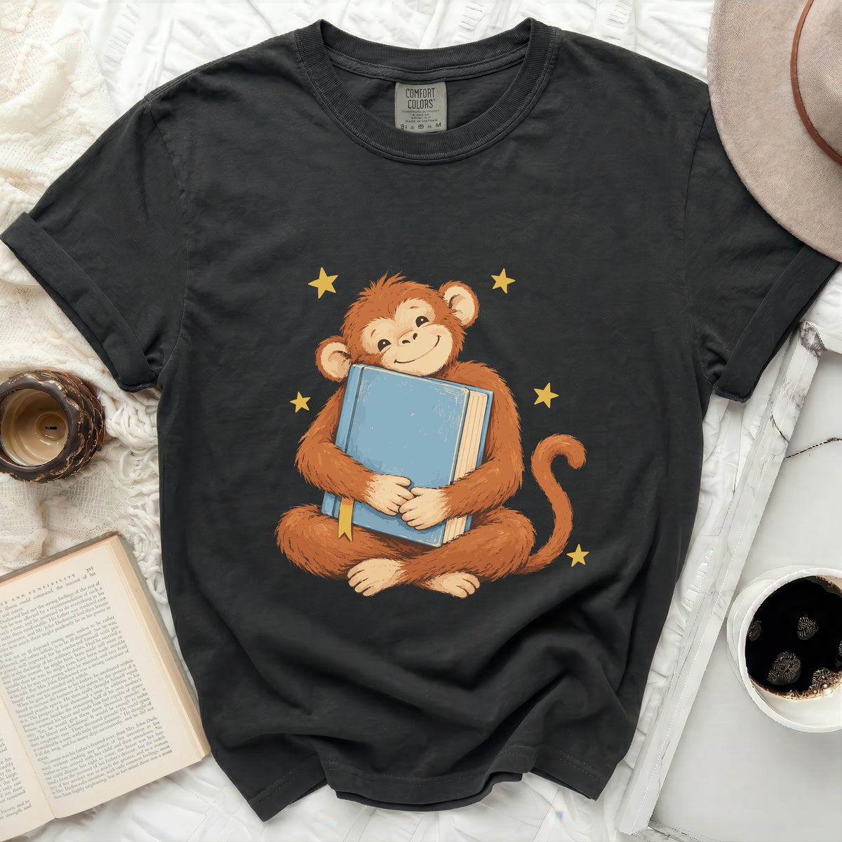 Dark grey t-shirt with a cheerful monkey hugging a blue book and yellow stars.