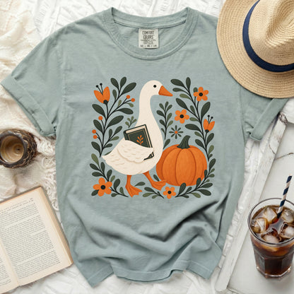 Light blue t-shirt with a goose holding a book amongst flowers and a pumpkin.