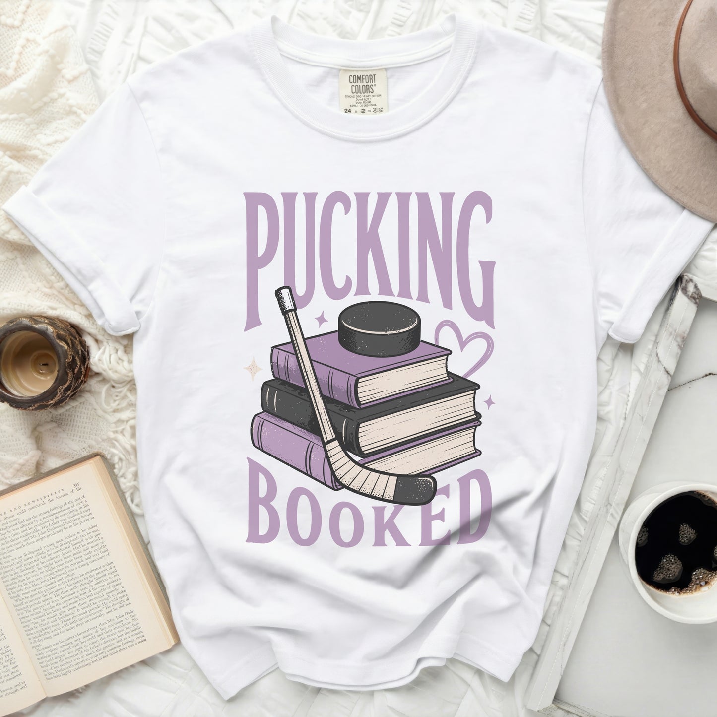 White t-shirt with "PuckING BOOKED" text and hockey puck on books.