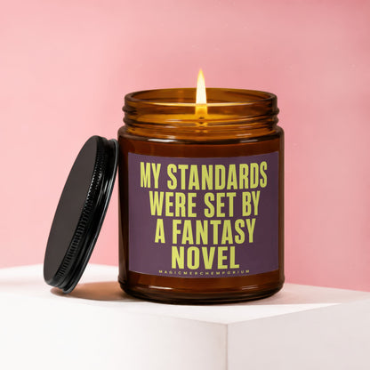 Amber jar candle with dark lid, lit flame, and text "My standards were set by a fantasy novel."