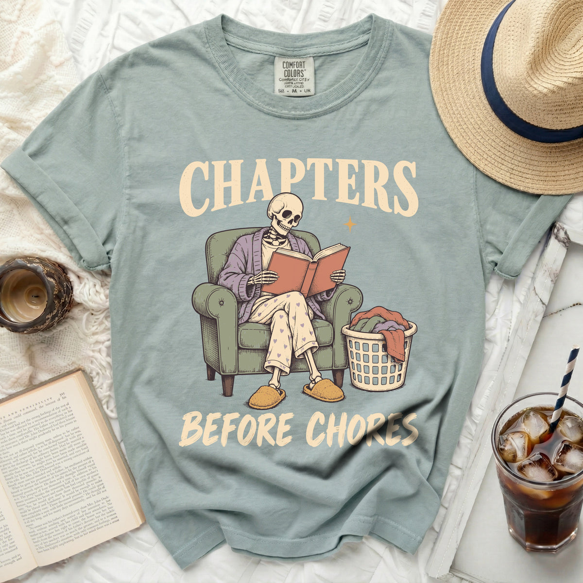 Skeleton reading in chair with laundry basket, text "Chapters Before Chores".